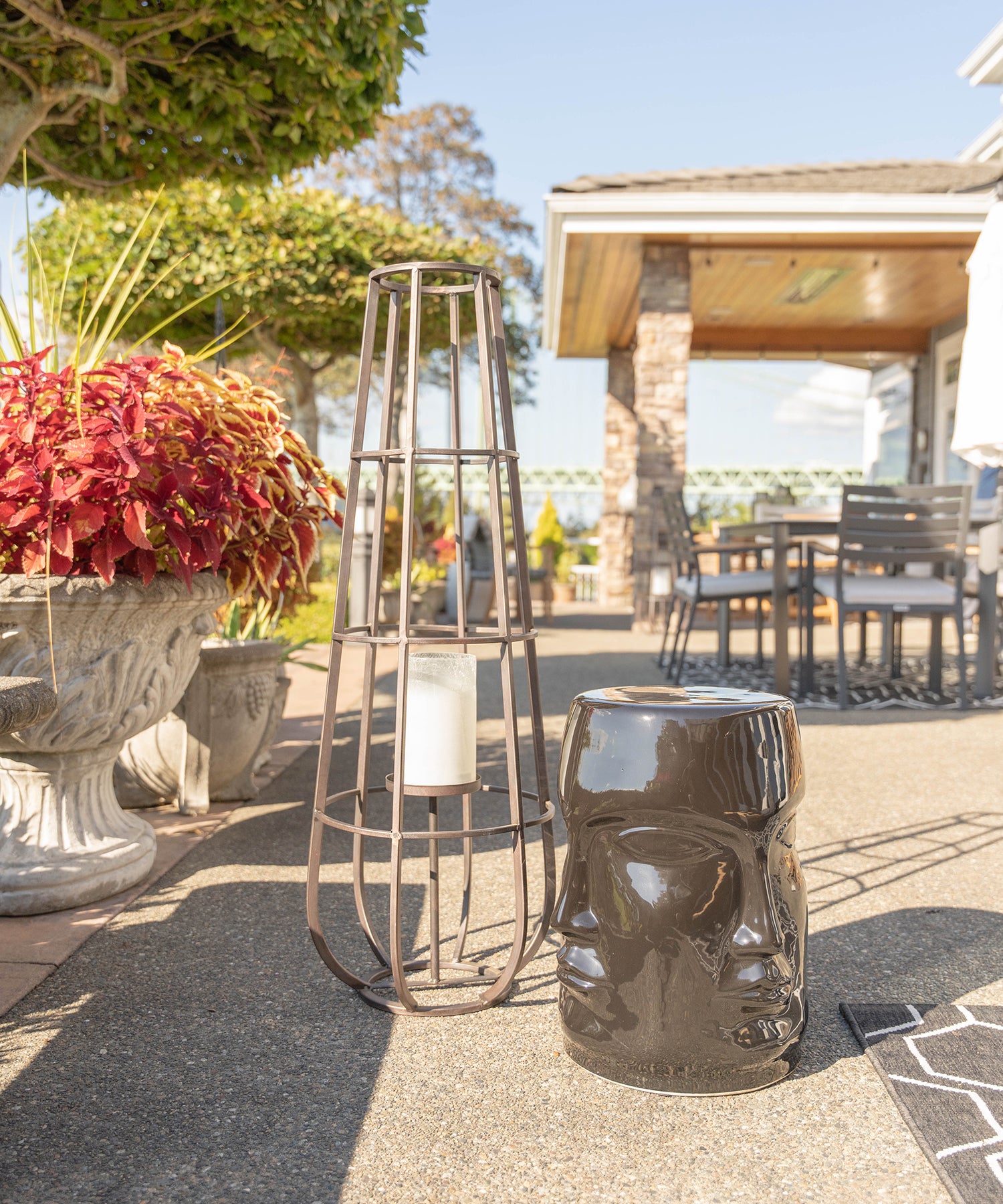 A metal lantern next to a black ceramic stool with faces on it on an outdoor patio area