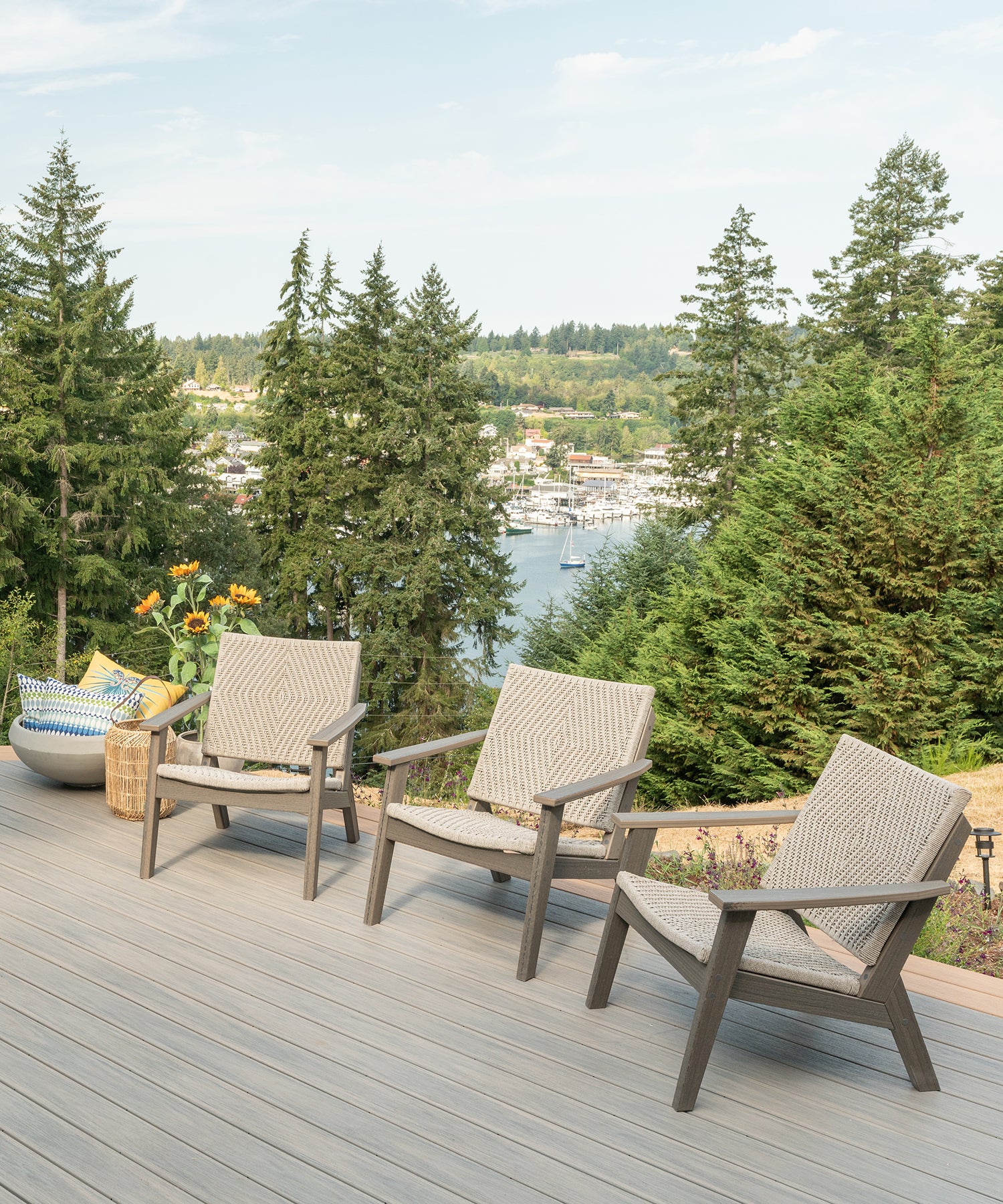 Three patio chairs on a deck overlooking a harbor with pine trees