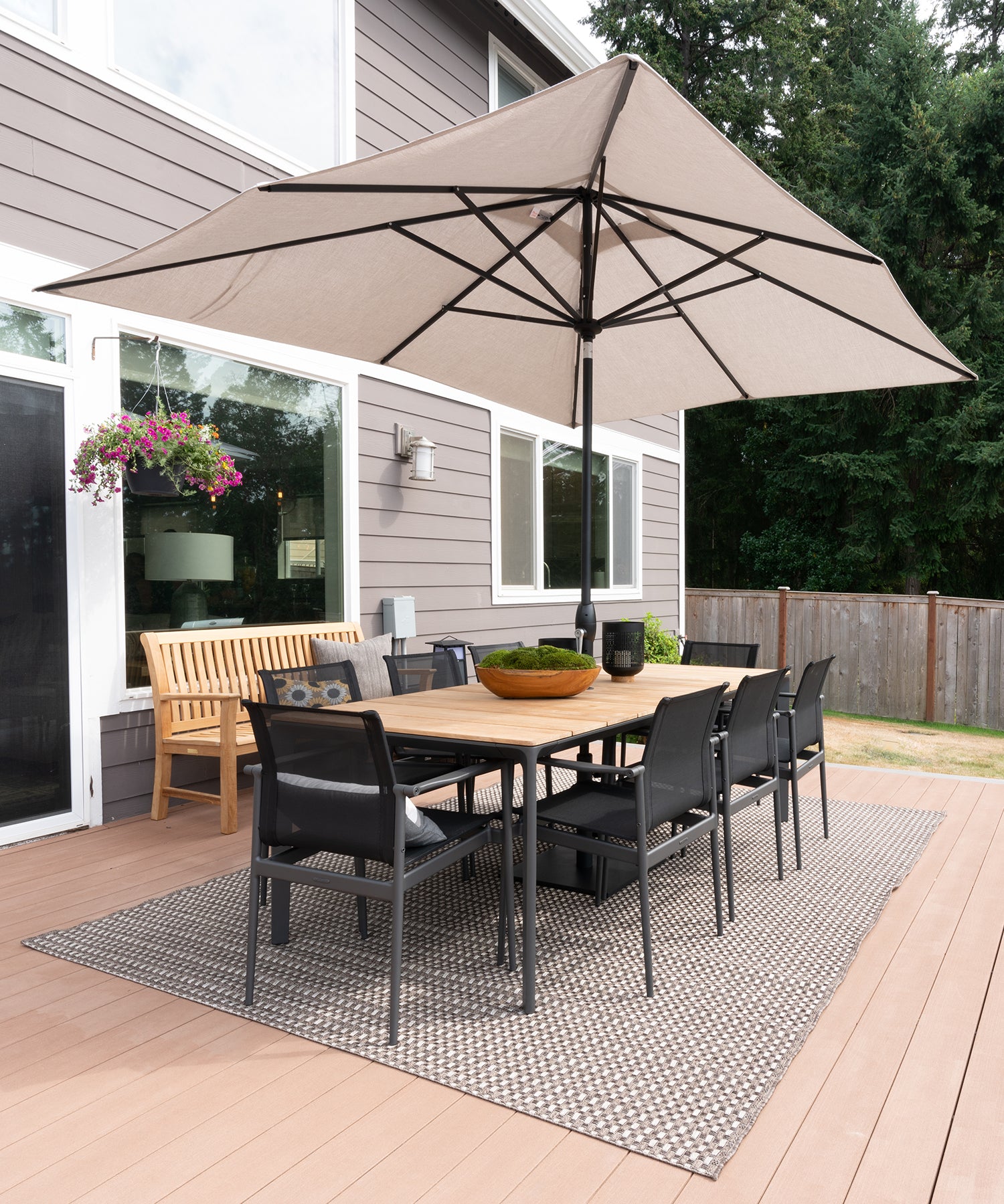Black outdoor dining chairs surrounding a teak outdoor dining table under an umbrella on a large porch