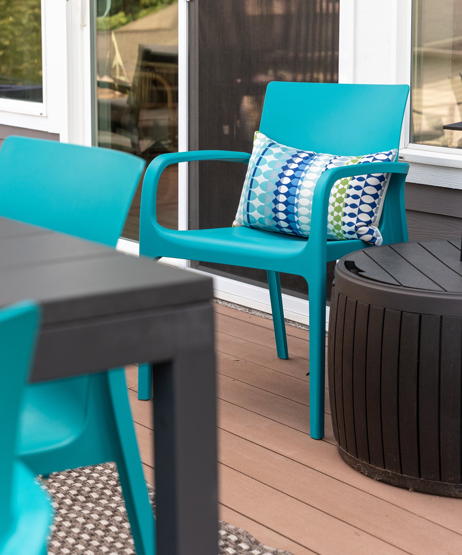 A blue plastic chair with a patterned pillow outside of a sliding glass door.