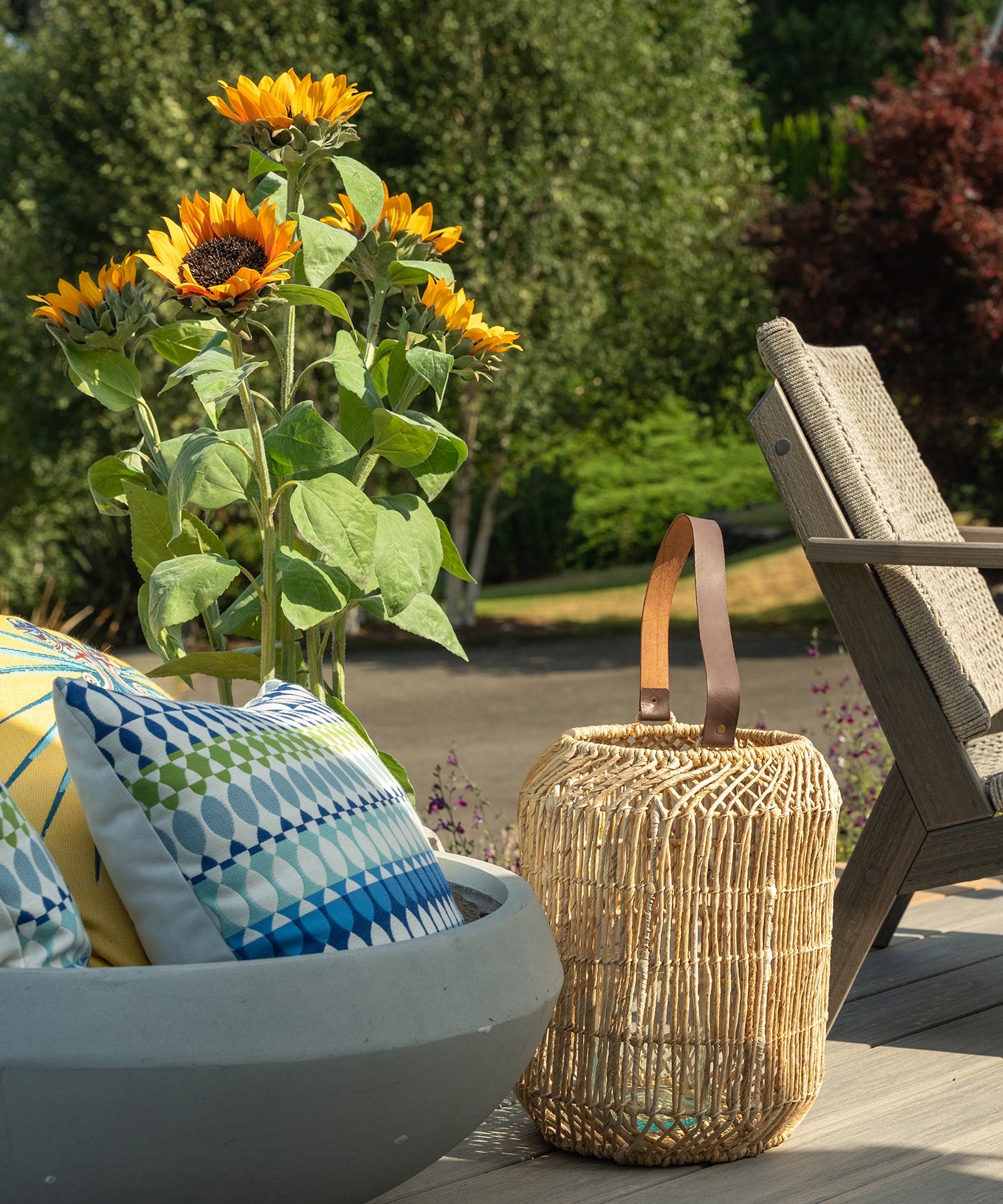 Outdoor patio with chair, woven basket, planter filled with pillows, and tall sunflowers.
