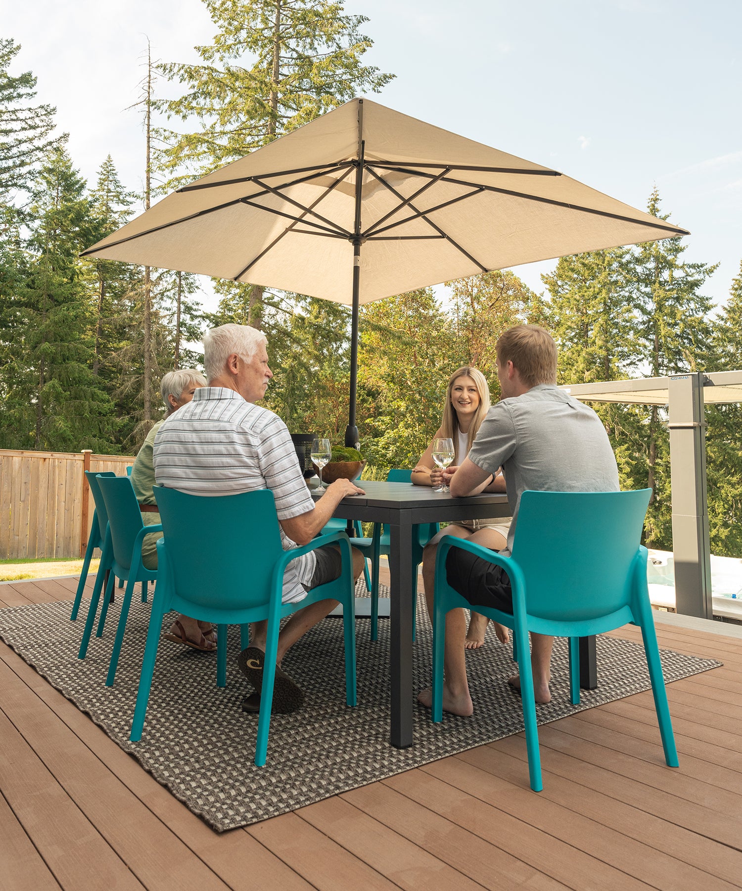 A group of people sitting around an outdoor dining table in blue chairs underneath an umbrella.