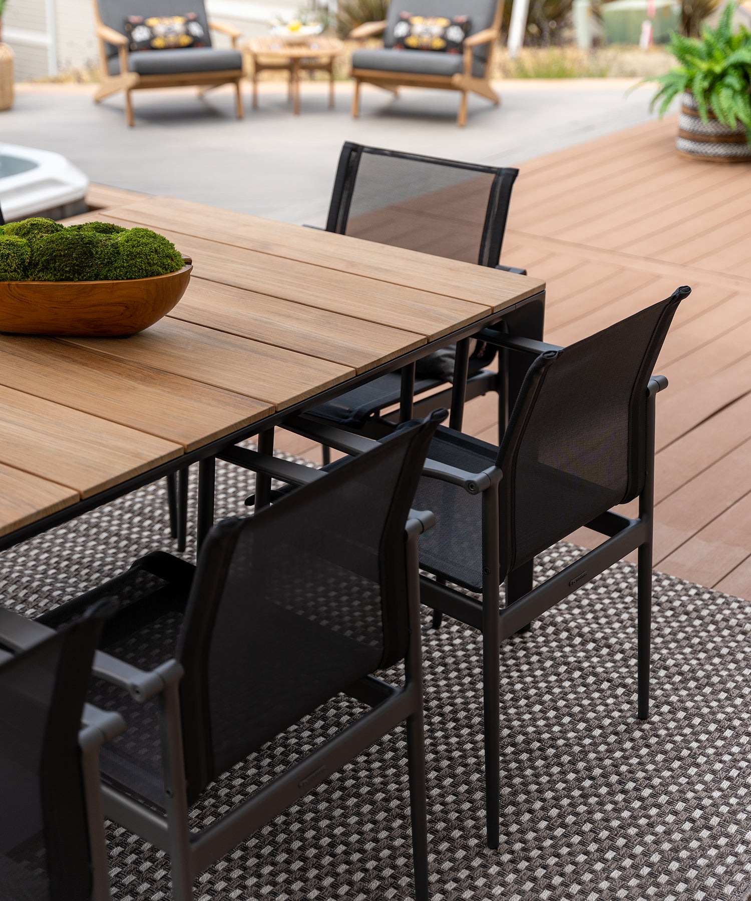 Close-up of black outdoor dining chairs around a teak top dining table on a porch