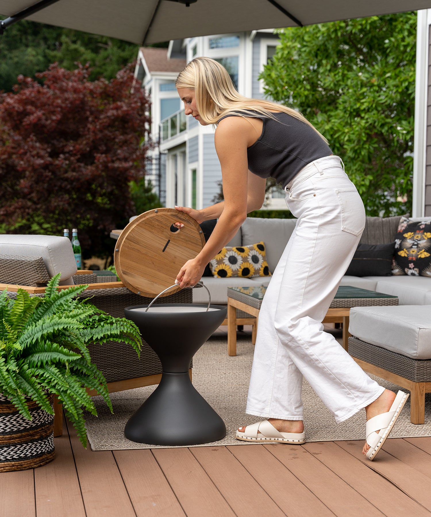A person lifting an ice bucket out of an outdoor side table on a porch